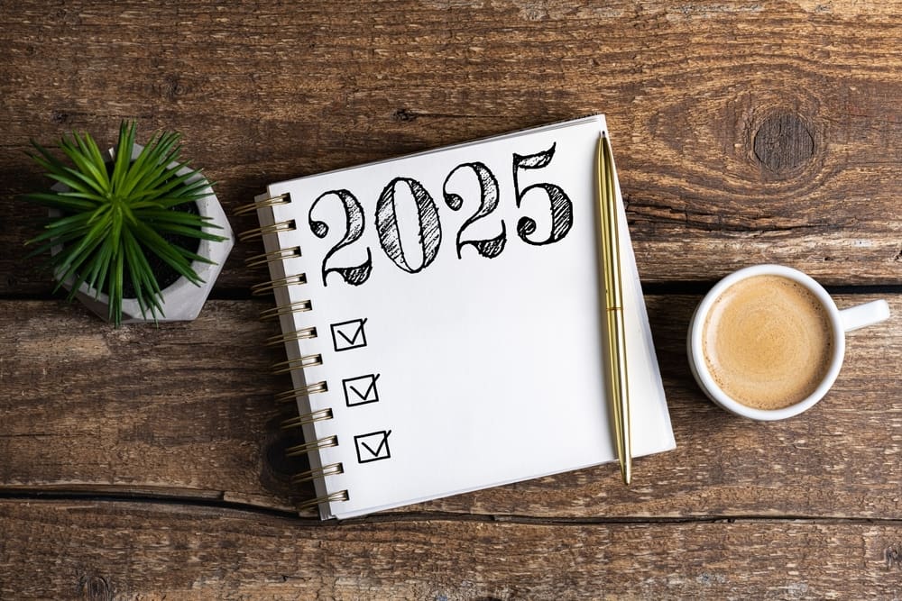 Notebook with 2025 writing on it, next to cup of coffee and plant